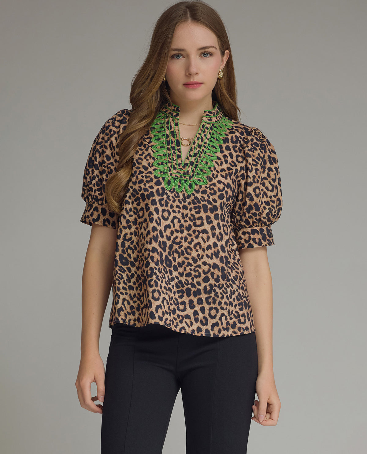 Woman wearing a leopard print blouse with green lace details on a gray background