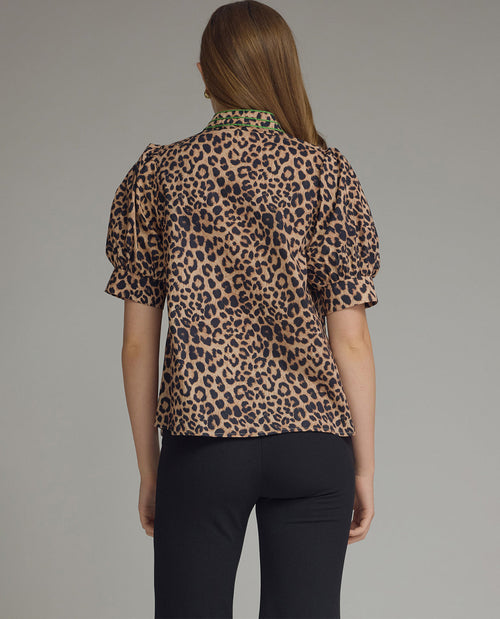 A woman viewed from the back wearing a leopard-print short-sleeve blouse with puff sleeves and black pants, against a plain gray studio background.