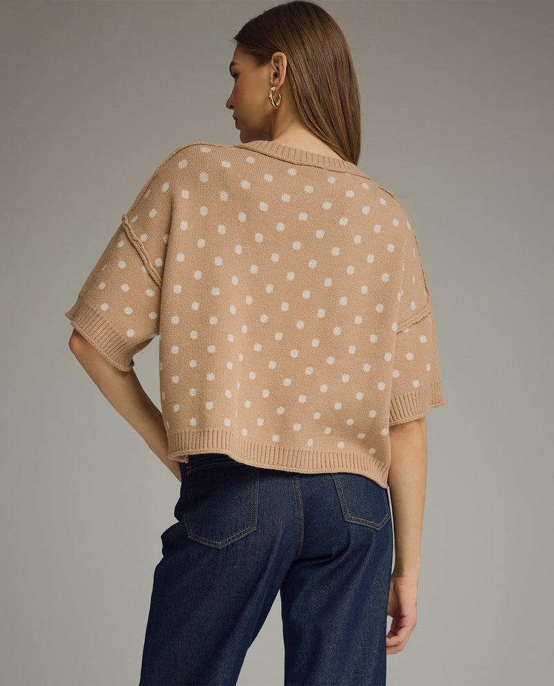 Woman wearing a beige polka dot top and blue jeans on a plain background