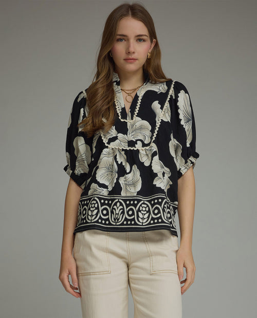 Woman wearing a black floral blouse with beige pants on a gray background