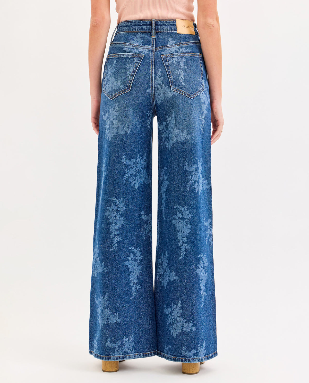 A model shown from the back wearing high-waisted, wide-leg blue denim jeans with a light blue floral or snowflake-like allover print. The shot is cropped from the waist down on a clean white studio background.