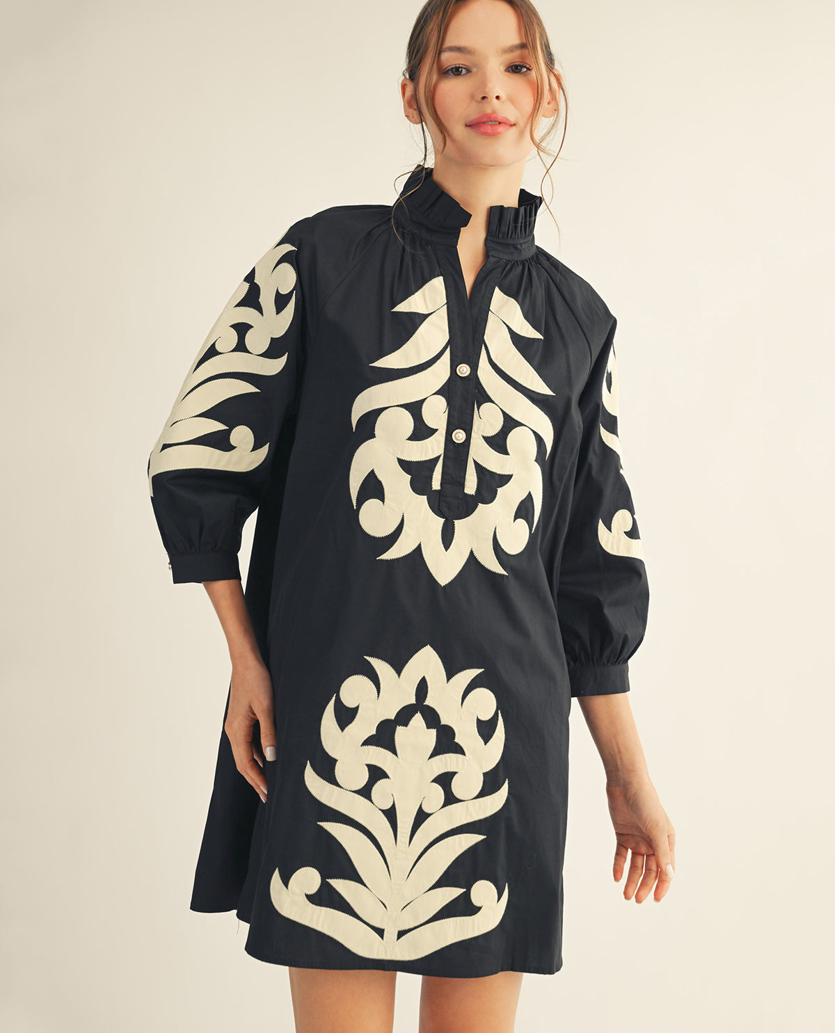 Woman wearing a black dress with white floral patterns on a beige background