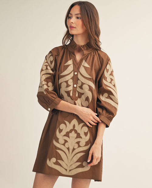 Woman wearing a brown dress with beige patterns on a plain background