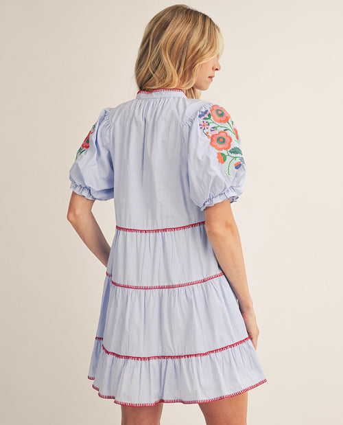 Woman wearing a light blue dress with floral embroidery on a beige background