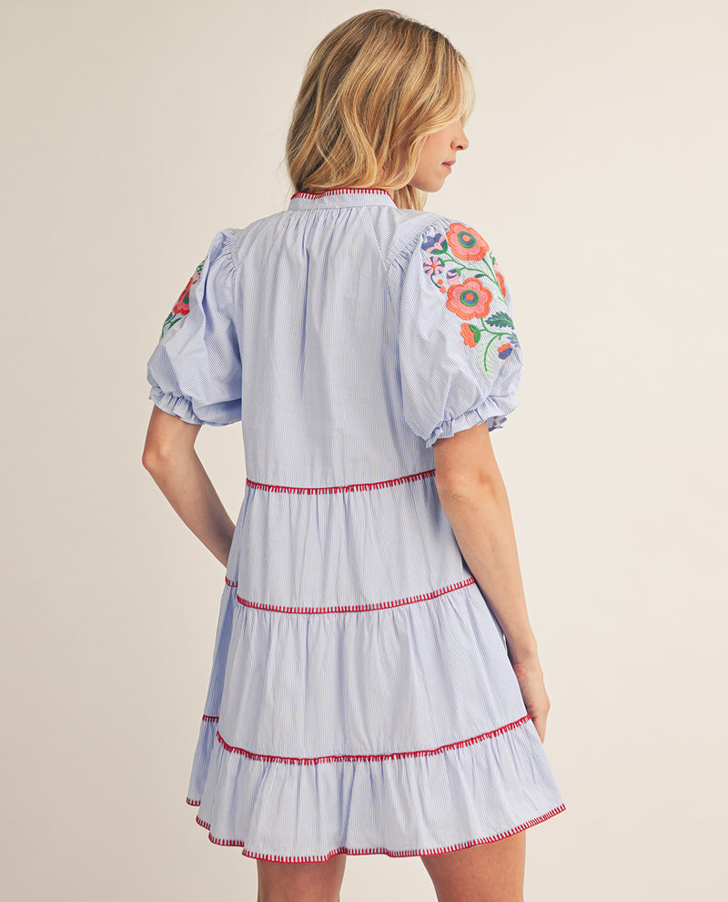 Woman wearing a light blue dress with floral embroidery on a beige background