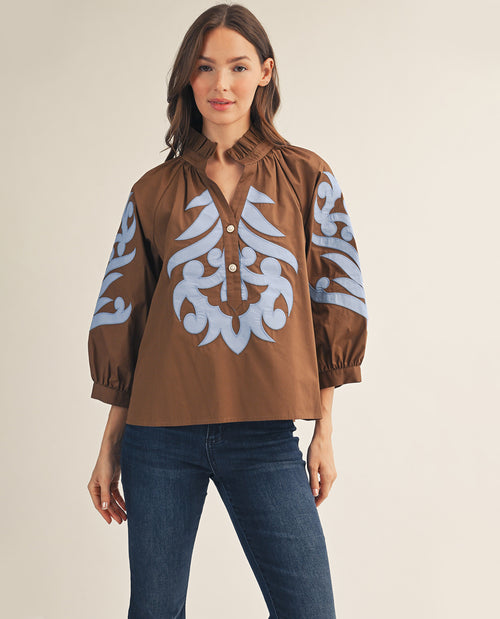 Woman wearing a brown blouse with blue patterns on a beige background