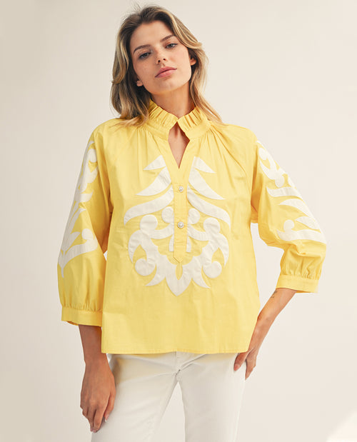Woman wearing a yellow blouse with white floral embroidery on a plain background