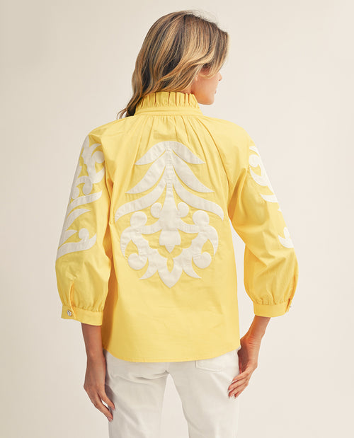 Woman wearing a yellow blouse with white embroidery on a beige background
