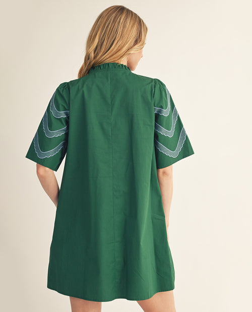 Green dress with white embroidery on sleeves worn by a person on a beige background