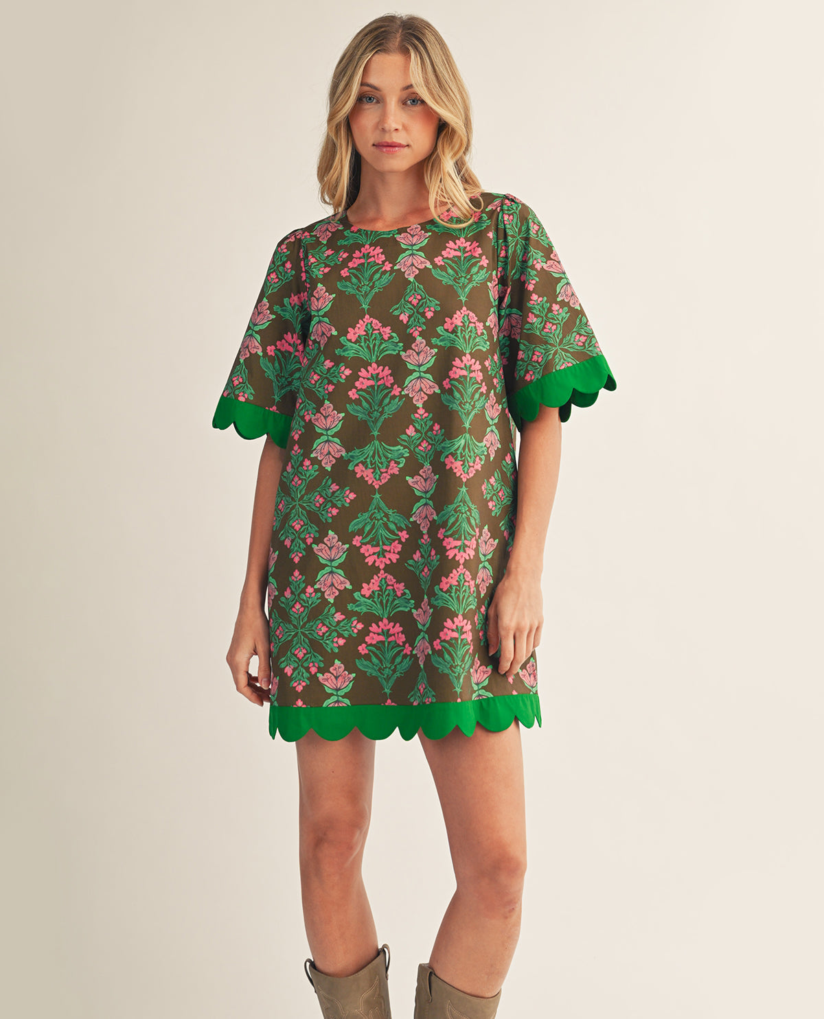 Woman wearing a floral dress with green trim on a plain background