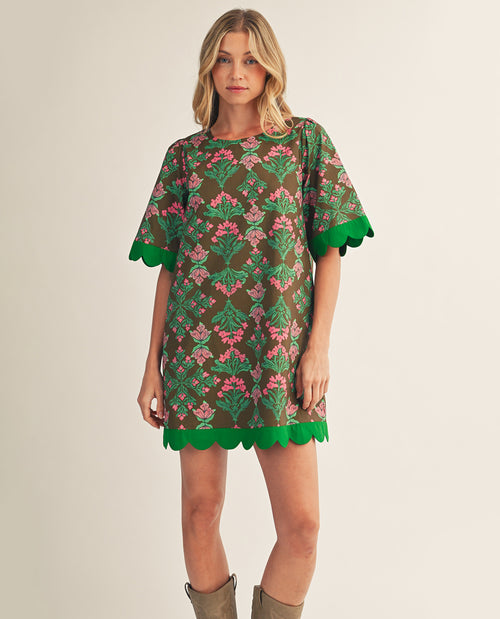 Woman wearing a floral dress with green trim on a plain background