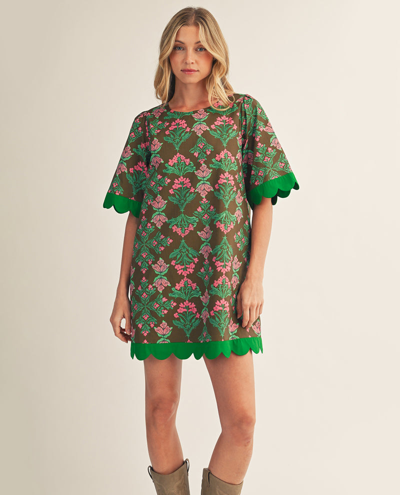 Woman wearing a floral dress with green trim on a plain background
