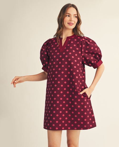 Woman wearing a maroon dress with pink polka dots on a beige background