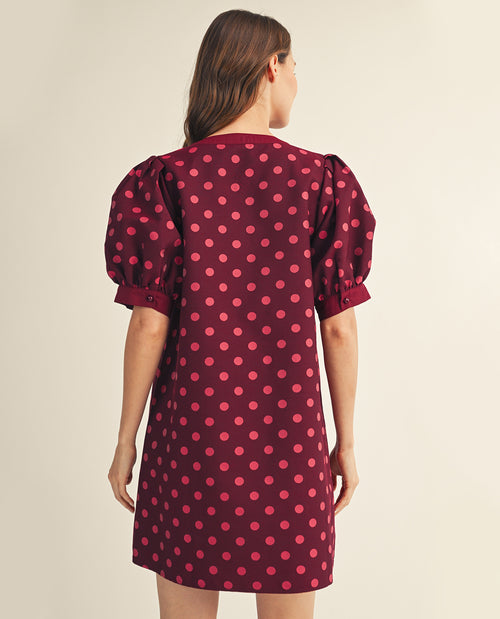 Woman wearing a maroon dress with pink polka dots from behind on a beige background