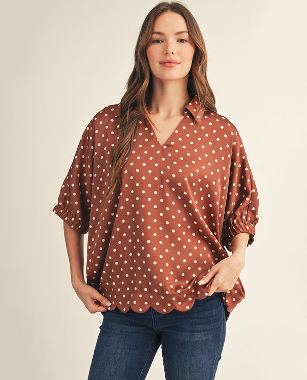 Woman wearing a brown polka dot blouse and blue jeans on a beige background