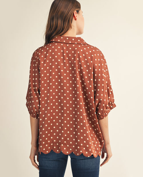 Woman wearing a brown polka dot blouse against a beige background