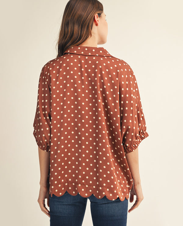 Woman wearing a brown polka dot blouse against a beige background