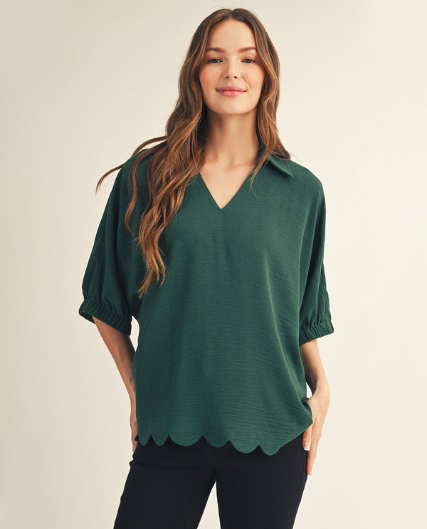 Woman wearing a green blouse with scalloped hem on a beige background