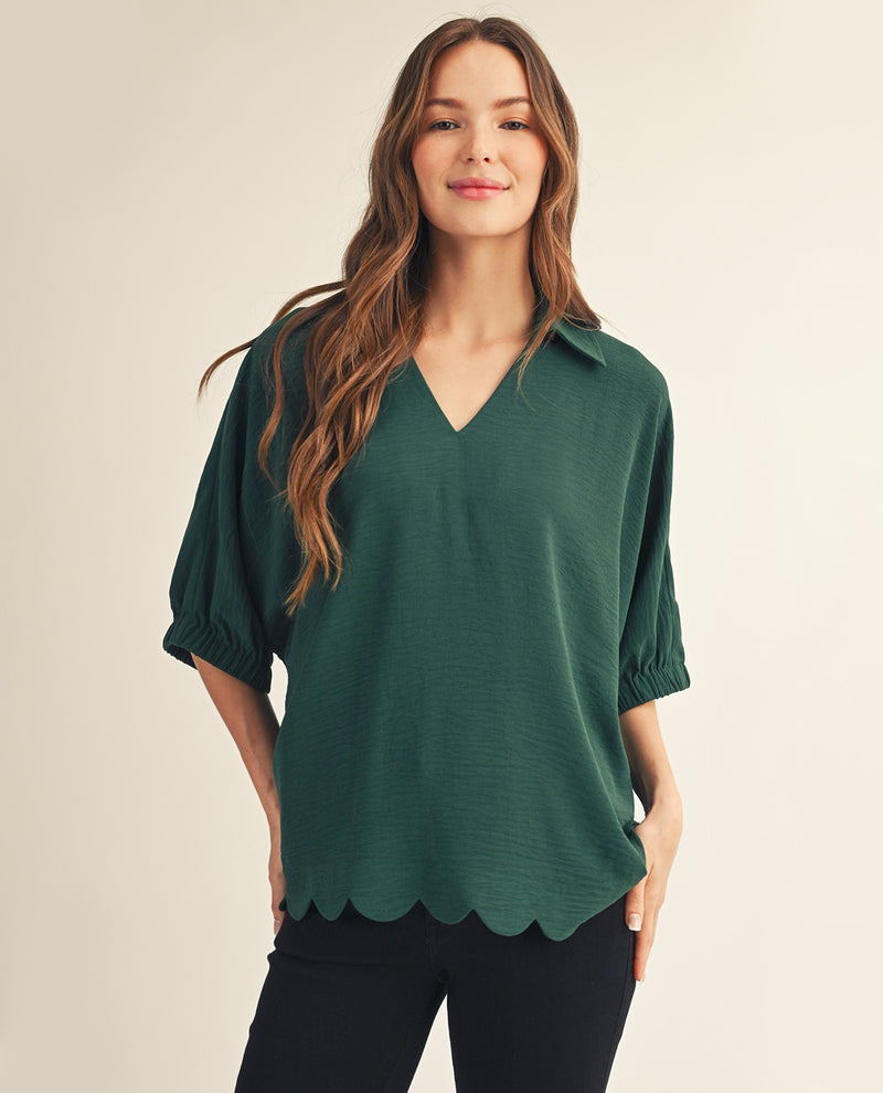 Woman wearing a green blouse with scalloped hem on a beige background