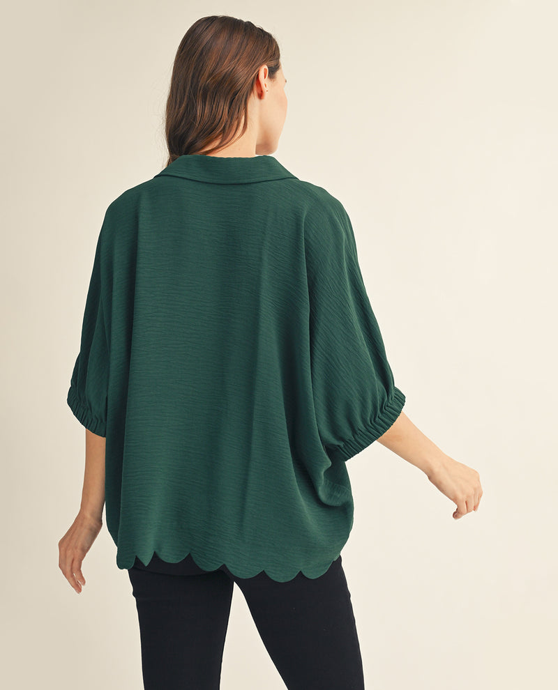 Woman wearing a green scalloped blouse against a beige background