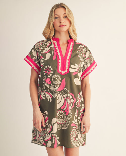 Woman wearing a patterned dress with pink accents on a plain background