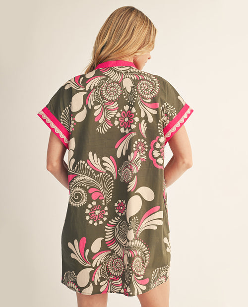 Woman wearing a floral patterned dress with pink accents on a plain background