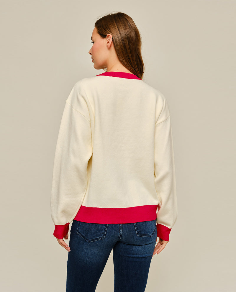 A woman shown from the back wearing a cream-colored crewneck sweatshirt with bright pink ribbed trim at the collar, cuffs, and hem, paired with blue jeans, against a solid light gray background.