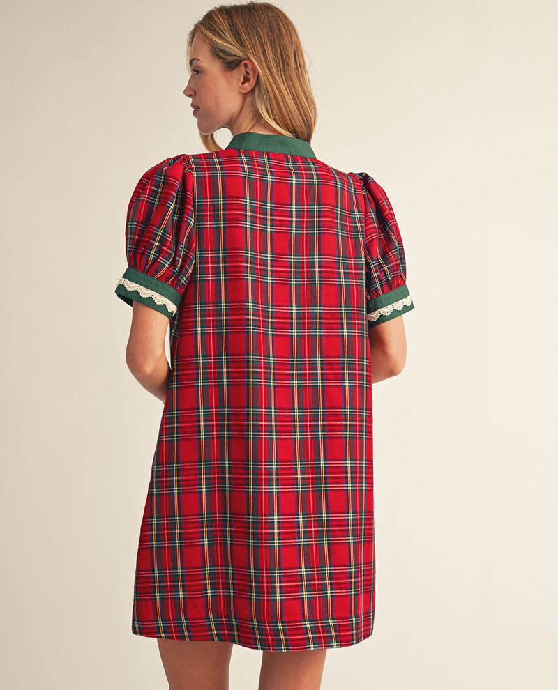 A woman shown from the back wearing a red tartan plaid dress with green trim on the collar and sleeve cuffs, featuring puffed short sleeves and a cream scalloped edge.