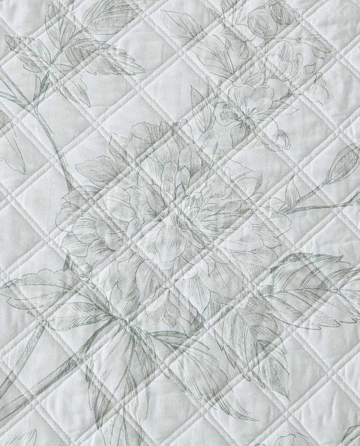 A close-up of a quilted fabric featuring a delicate, tonal floral pattern in light gray on an off-white background.
