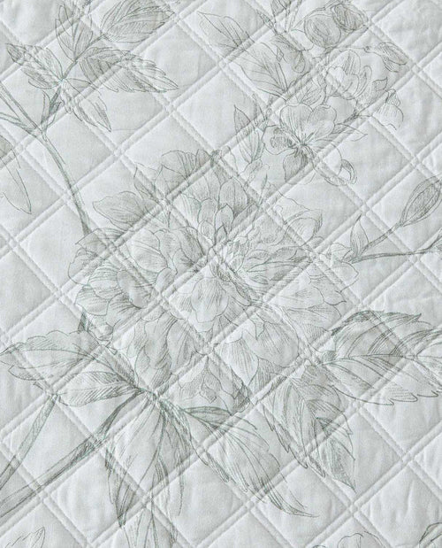 A close-up of a quilted fabric featuring a delicate, tonal floral pattern in light gray on an off-white background.