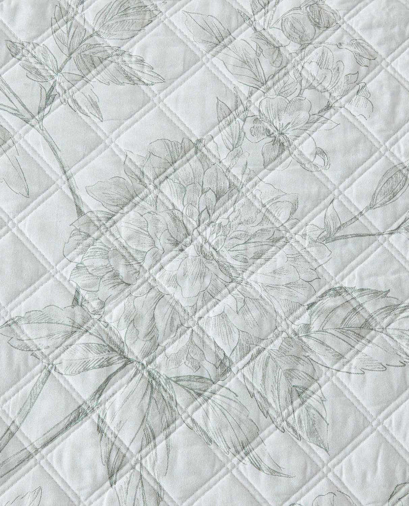 A close-up of a quilted fabric featuring a delicate, tonal floral pattern in light gray on an off-white background.