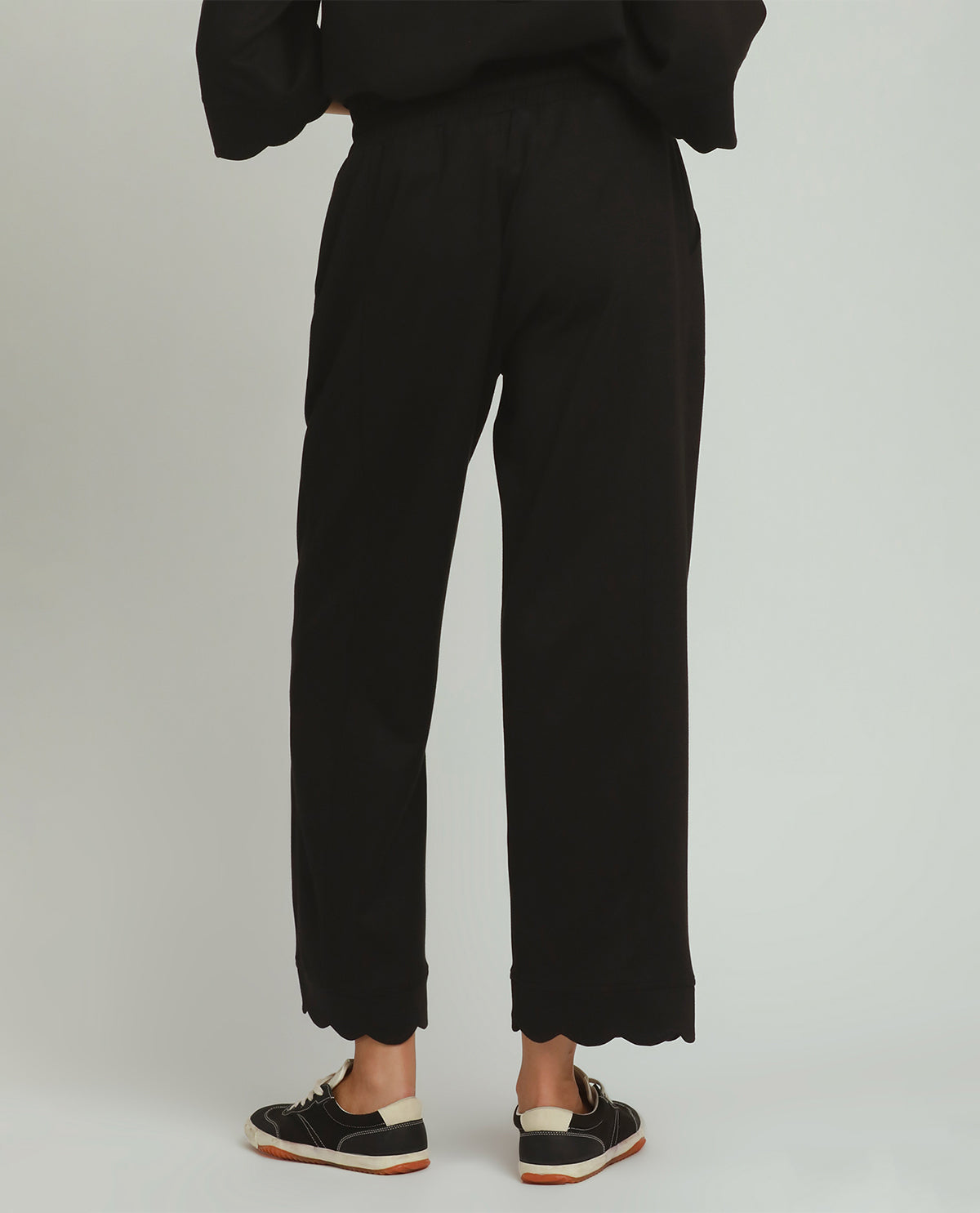 Black wide-leg cropped pants shown from the back on a model, paired with black sneakers, against a light gray studio background.