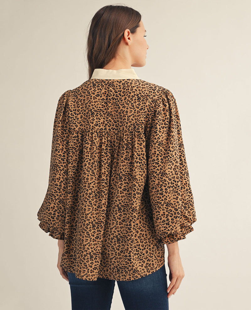 A woman shown from the back wearing a leopard-print blouse with a cream collar and blue jeans, against a plain light beige studio background.