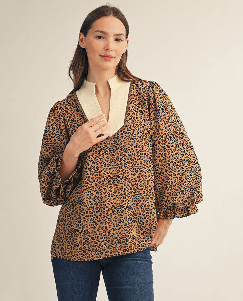 A woman shown from the front wearing a leopard-print blouse with a cream collar and blue jeans, against a plain light beige studio background.
