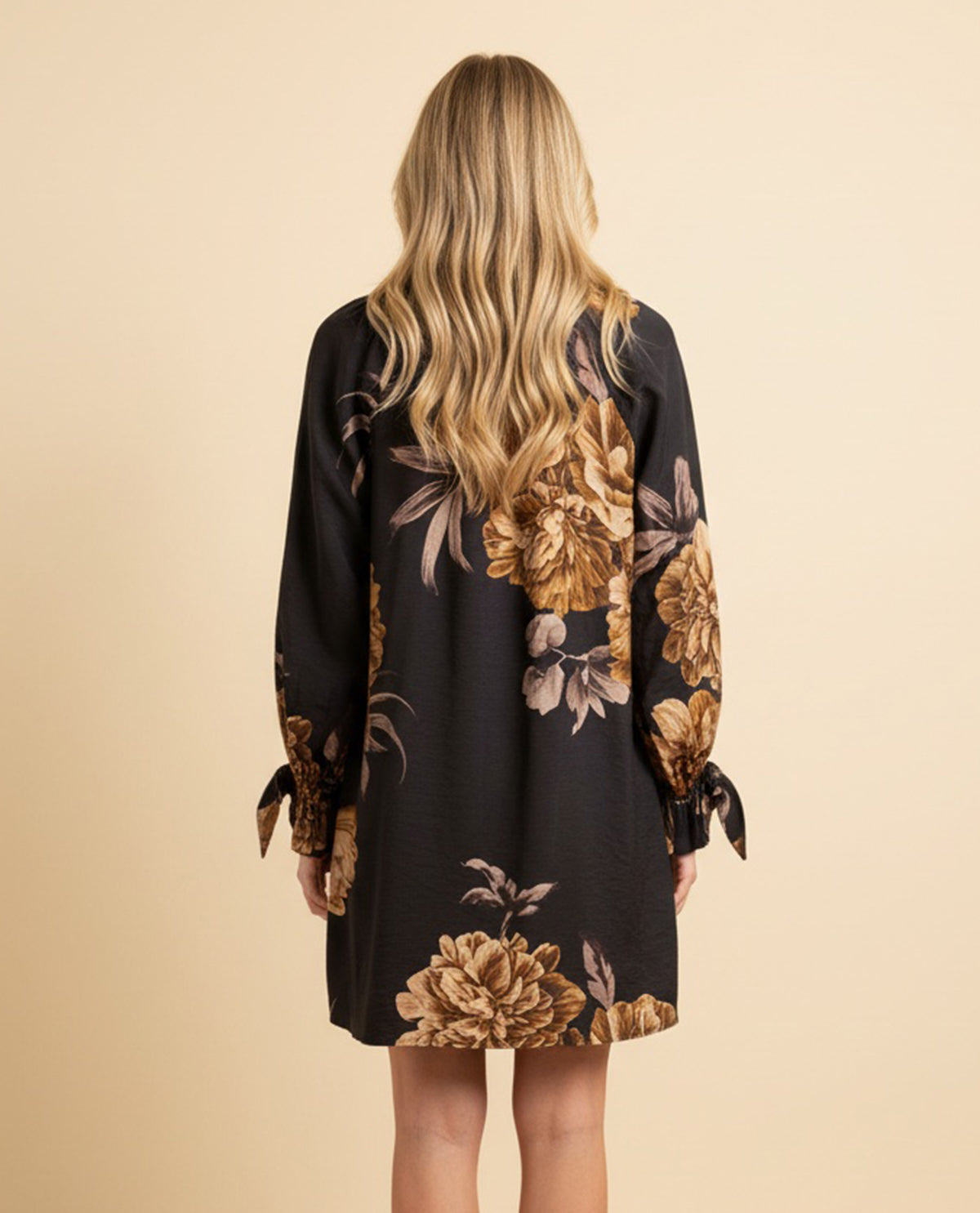 Woman wearing a black dress with gold floral patterns on a beige background