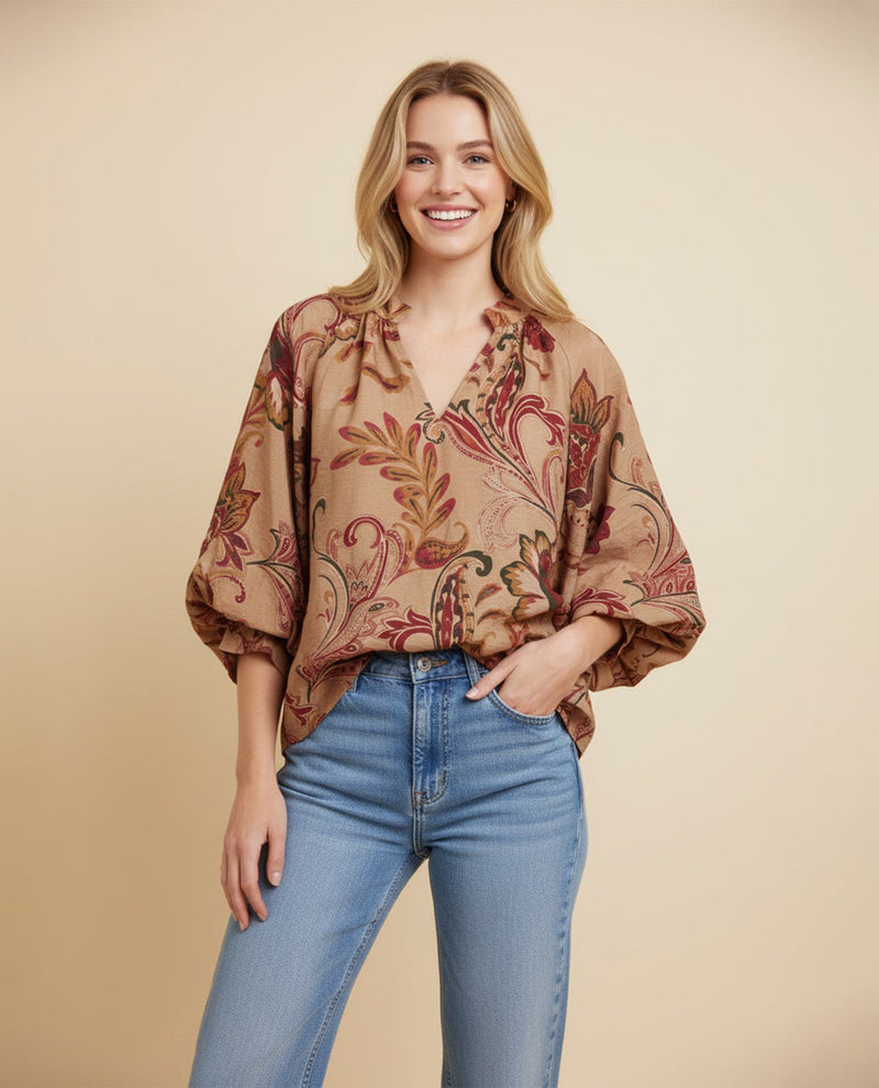 Woman wearing a patterned blouse and jeans against a beige background
