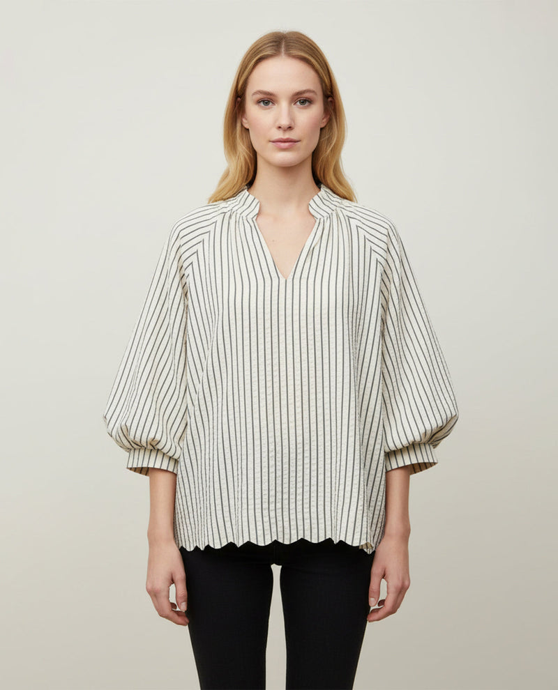 A woman modeling a cream-colored blouse with thin black vertical stripes, featuring a split collar, a split V-neckline, and voluminous elbow-length puff sleeves. She is also wearing black pants, set against a plain light gray studio background.