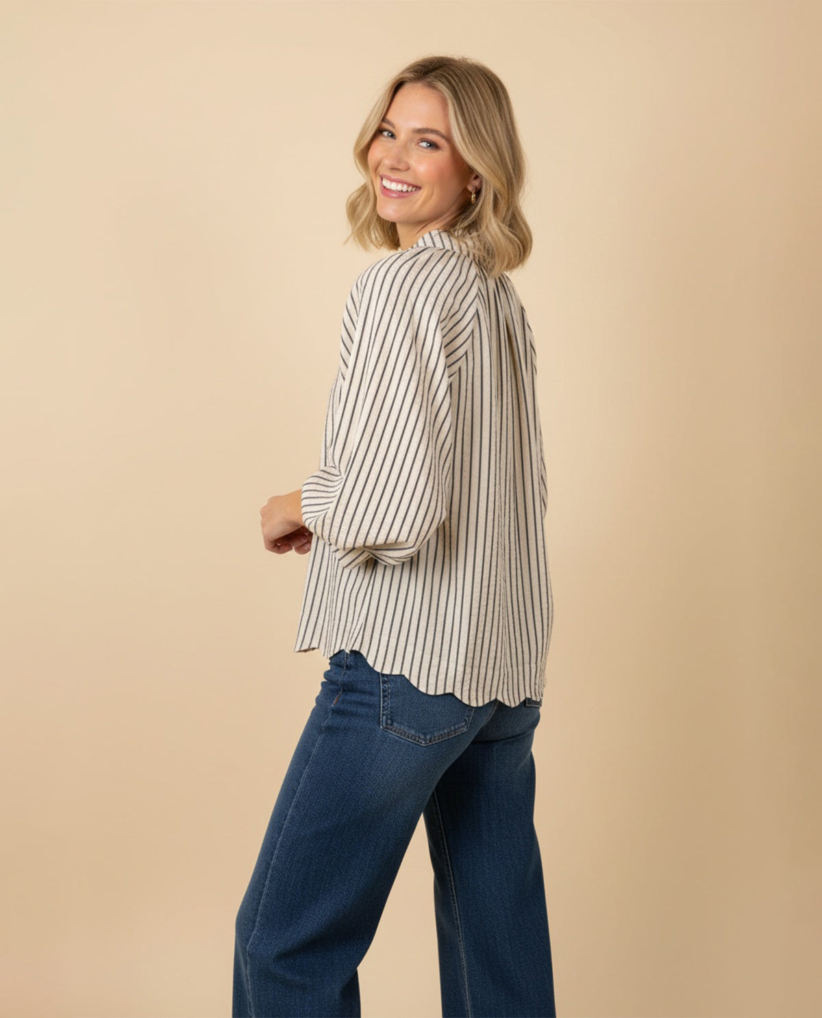 Woman wearing a striped blouse and blue jeans against a beige background