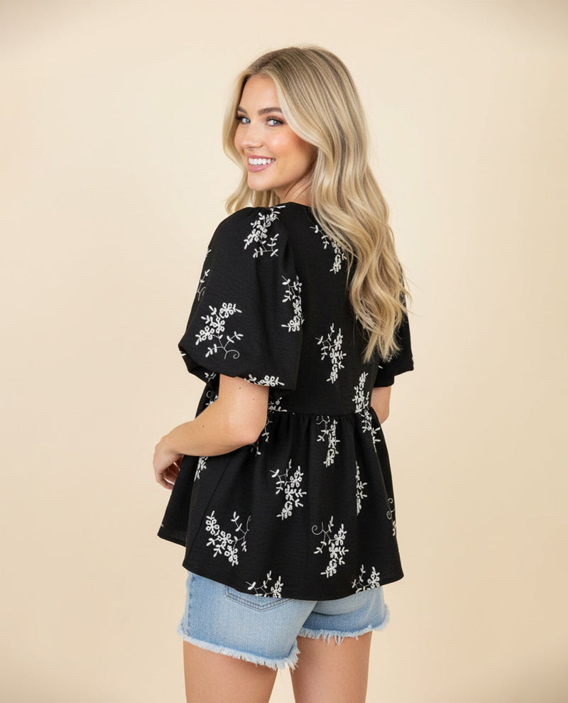 Woman wearing a black floral blouse with denim shorts on a beige background