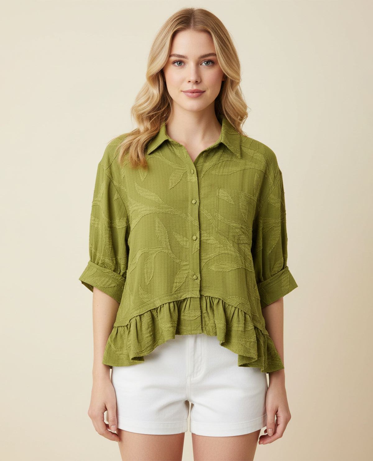 Woman wearing a green ruffled blouse and white shorts on a beige background