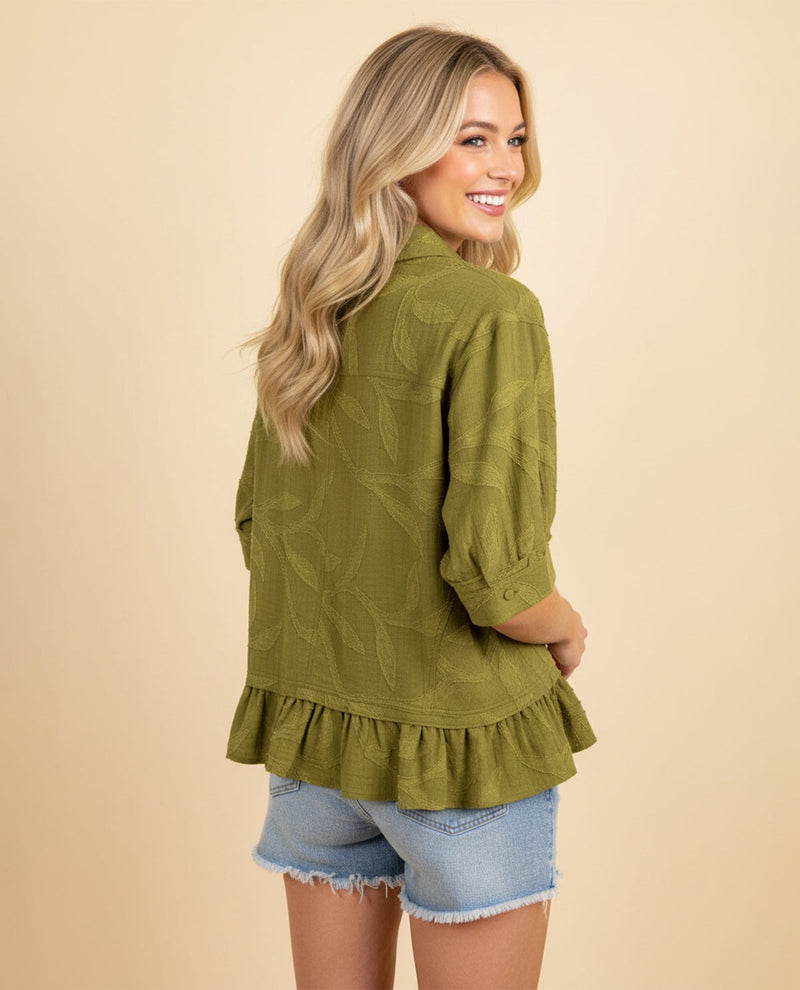 Woman wearing a green ruffled blouse and denim shorts on a beige background