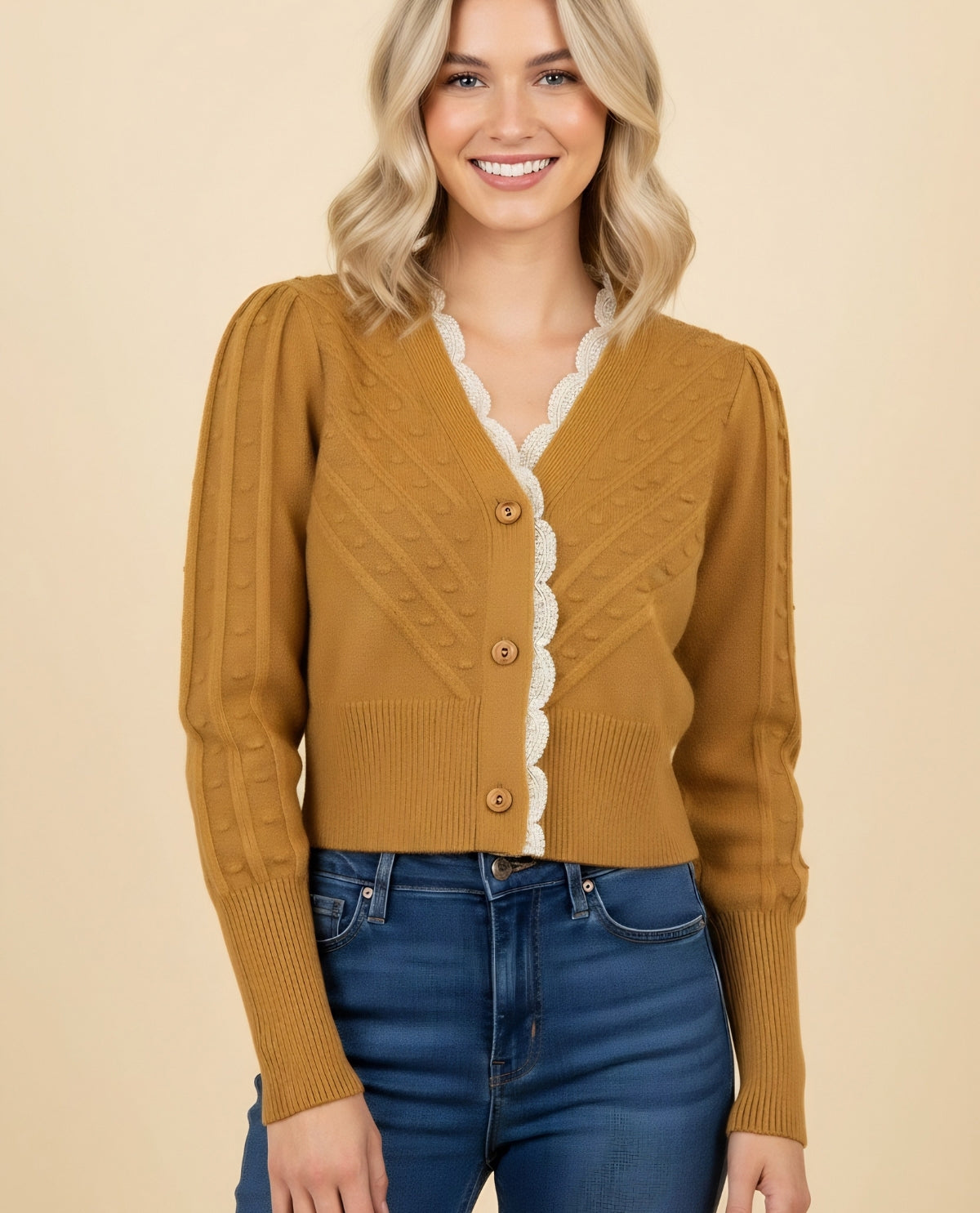 Woman wearing a mustard yellow cardigan with lace trim on a beige background