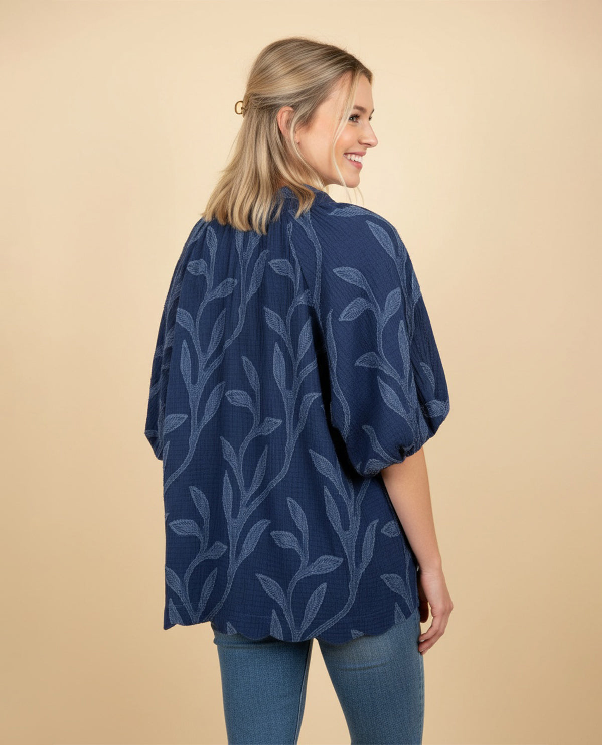 A woman wearing a navy blue short-sleeve blouse with a light blue leaf pattern, shown from the back against a solid beige background.