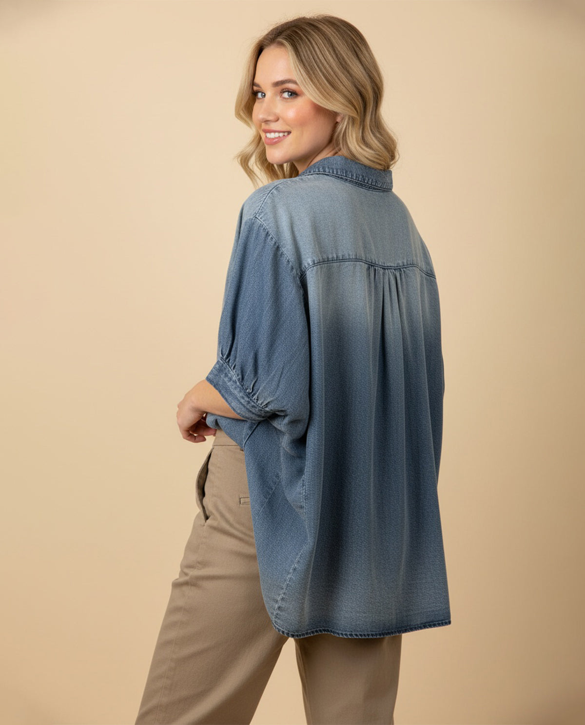 Woman wearing a blue denim shirt and beige pants on a beige background