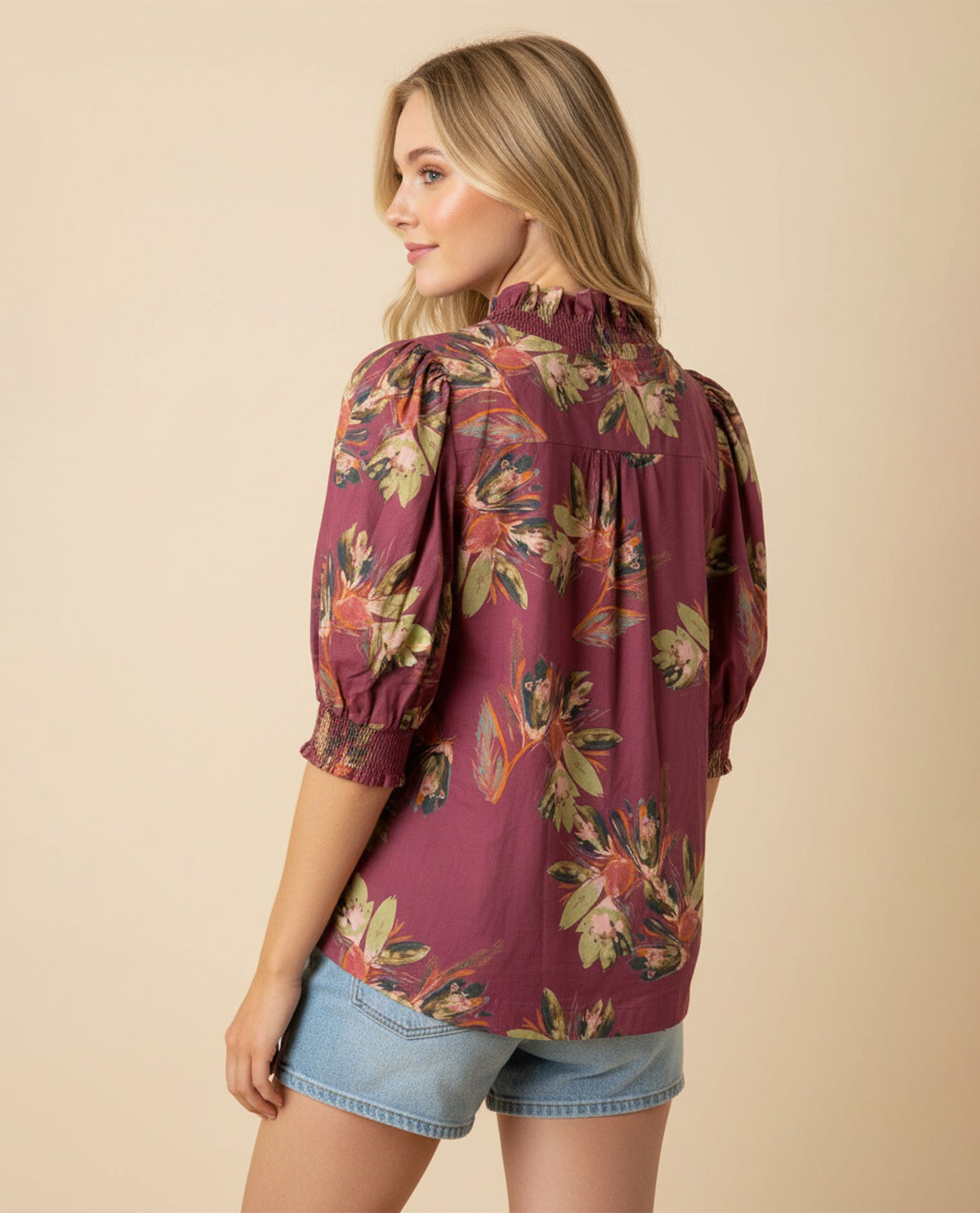 Woman wearing a burgundy floral blouse with denim shorts on a beige background