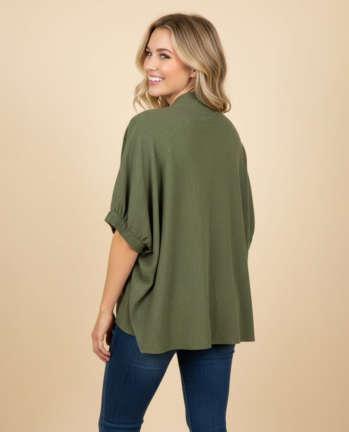 Woman wearing an olive green sweater and blue jeans on a beige background