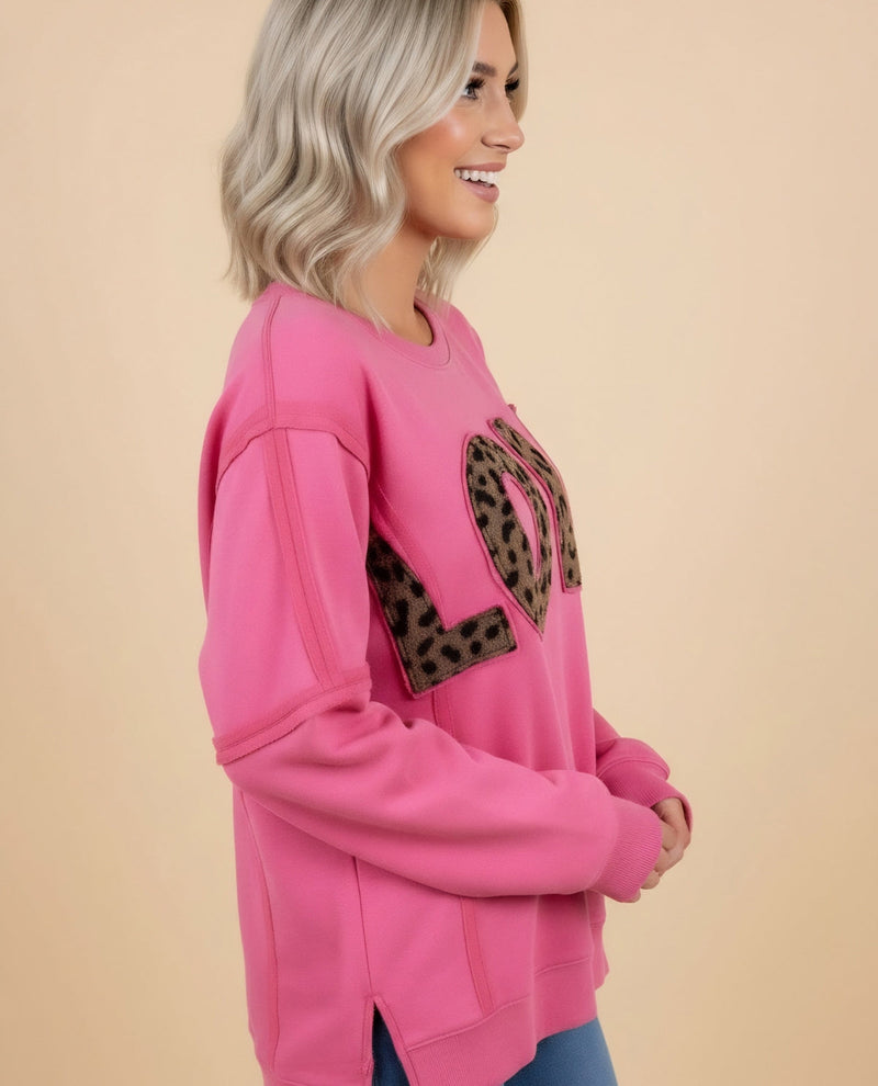 Woman wearing a pink sweatshirt with a leopard print heart design on a beige background