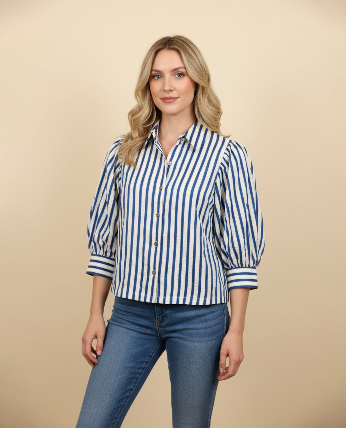 Woman wearing a blue and white striped shirt and jeans on a beige background