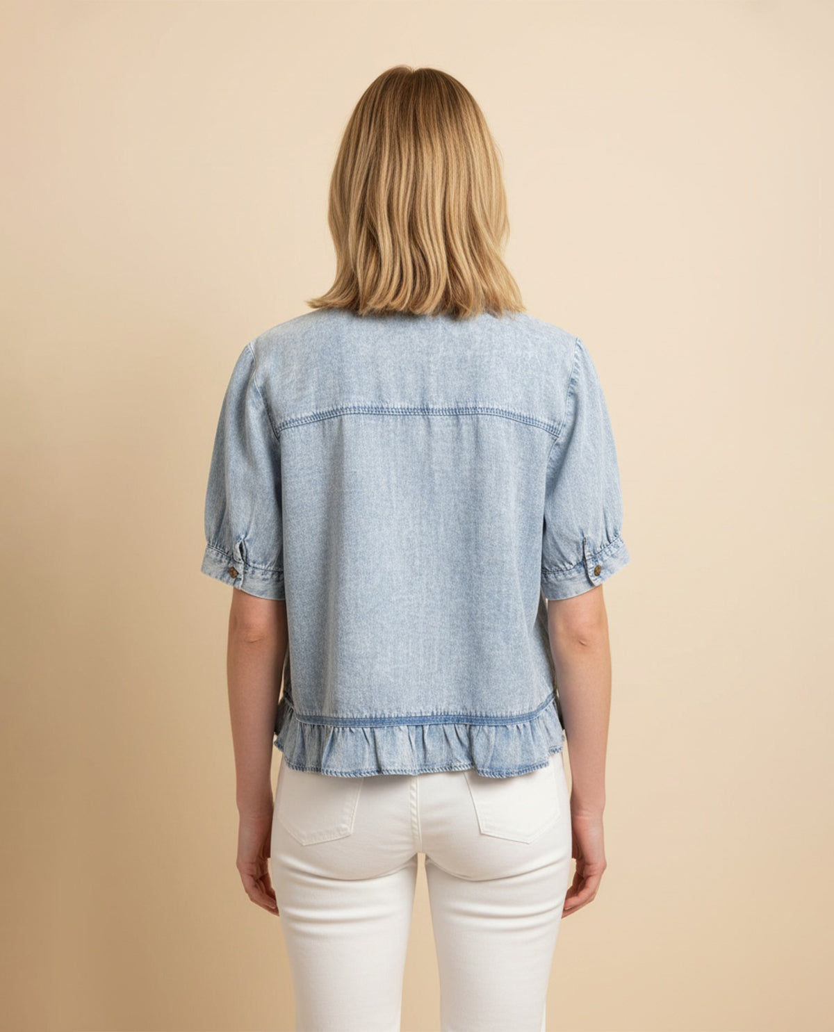 Person wearing a light blue denim shirt with ruffled hem on a beige background
