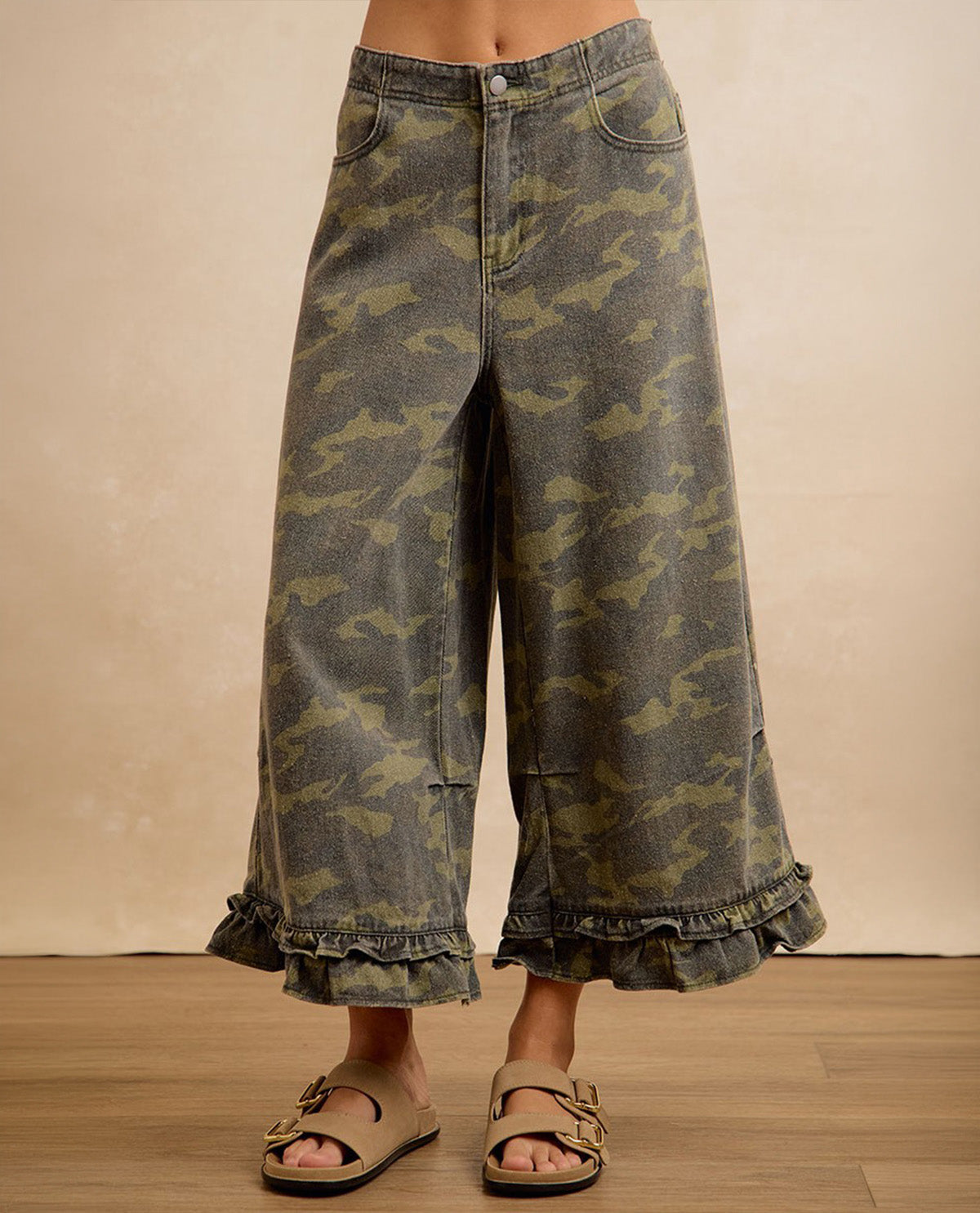 Camouflage wide-leg pants worn by a person on a wooden floor with a beige wall background